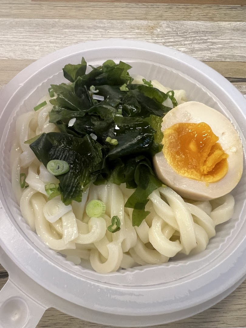 A close-up of a bowl of udon noodles topped with seaweed, green onions, and a soft-boiled egg.