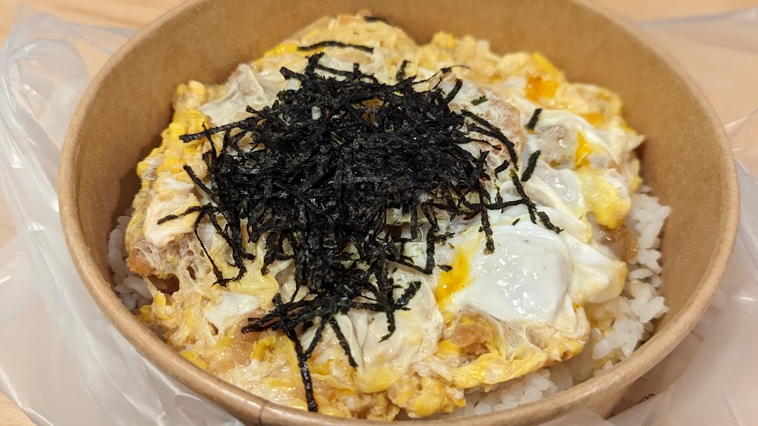 A close-up of a delicious Japanese-style rice bowl with egg, meat, and shredded seaweed in a paper bowl.