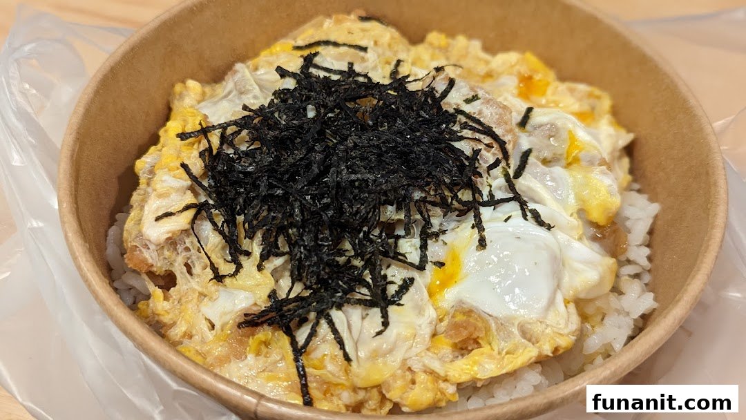 A close-up of a delicious Japanese-style rice bowl with egg, meat, and shredded seaweed in a paper bowl.
