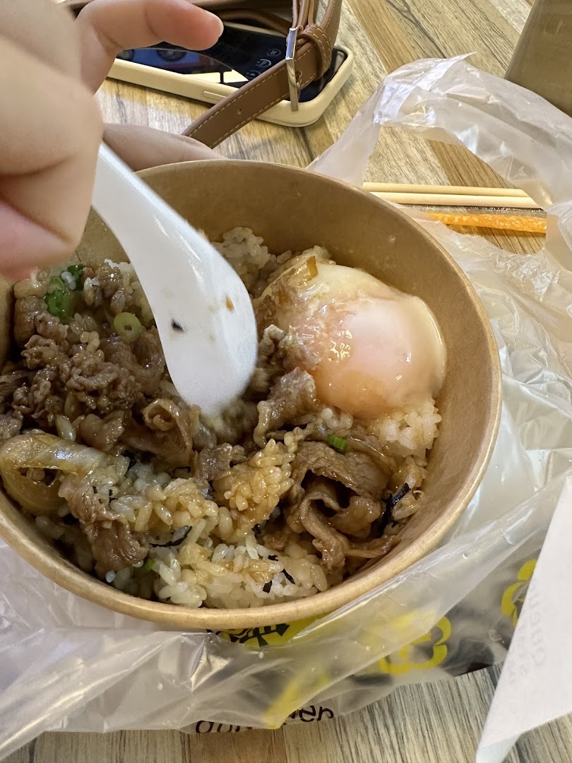 A close-up of a delicious beef and rice bowl with a soft-boiled egg, being enjoyed with a spoon.