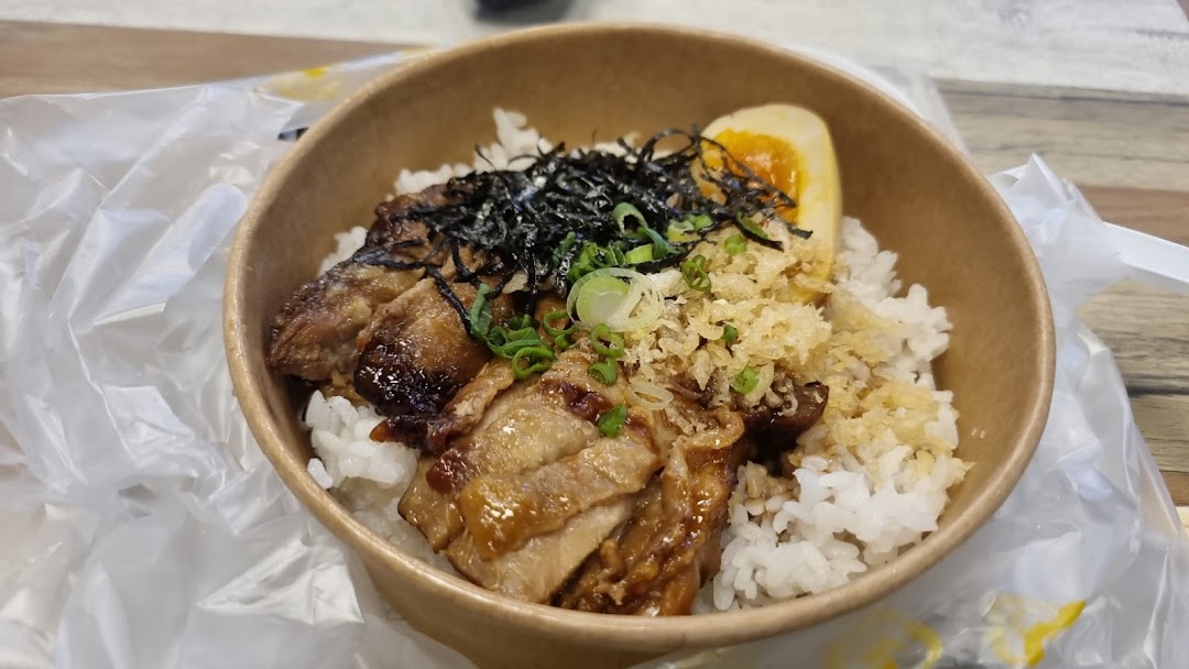 A close-up of a delicious rice bowl with grilled meat, a soft-boiled egg, and various toppings.