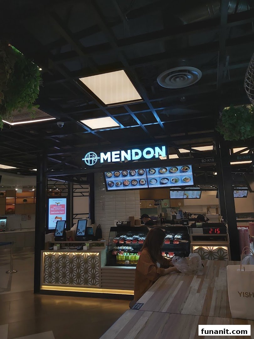 The Mendon shop counter with a digital menu board, food displays, and a customer in a modern setting.