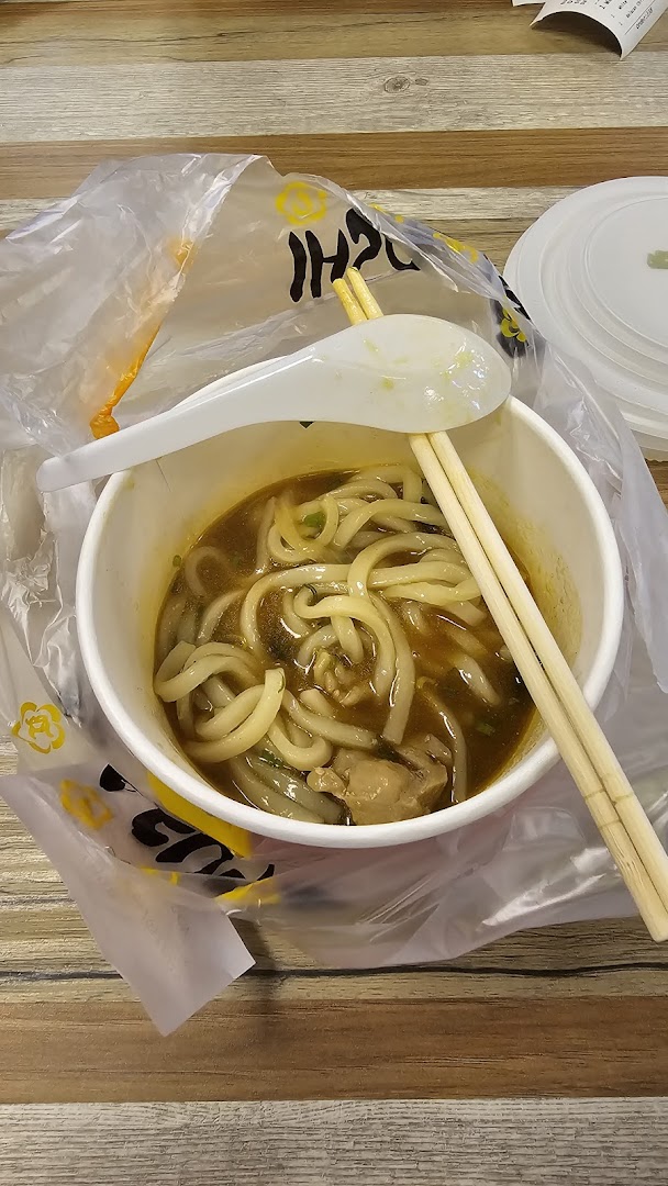 A close-up of a delicious bowl of noodles with broth, chopsticks, and a spoon on a wooden table.