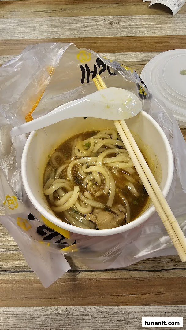 A close-up of a delicious bowl of noodles with broth, chopsticks, and a spoon on a wooden table.
