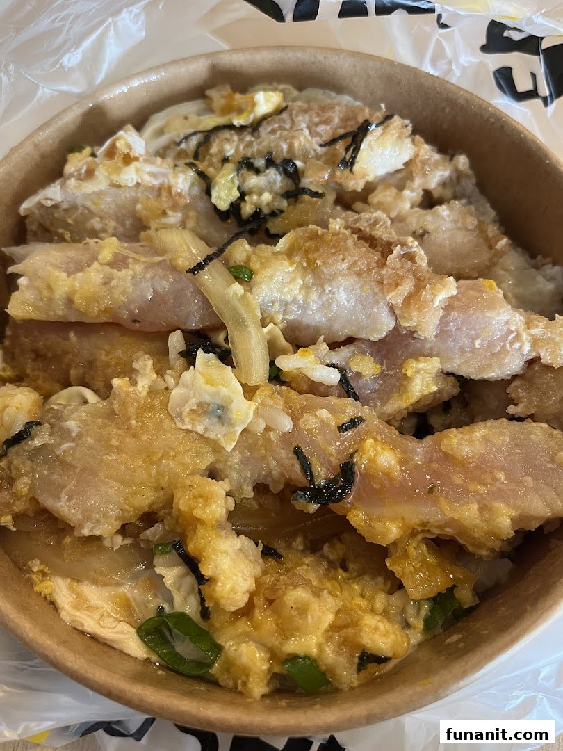 A close-up of a delicious donburi bowl featuring crispy fried protein, scrambled egg, and green onions.