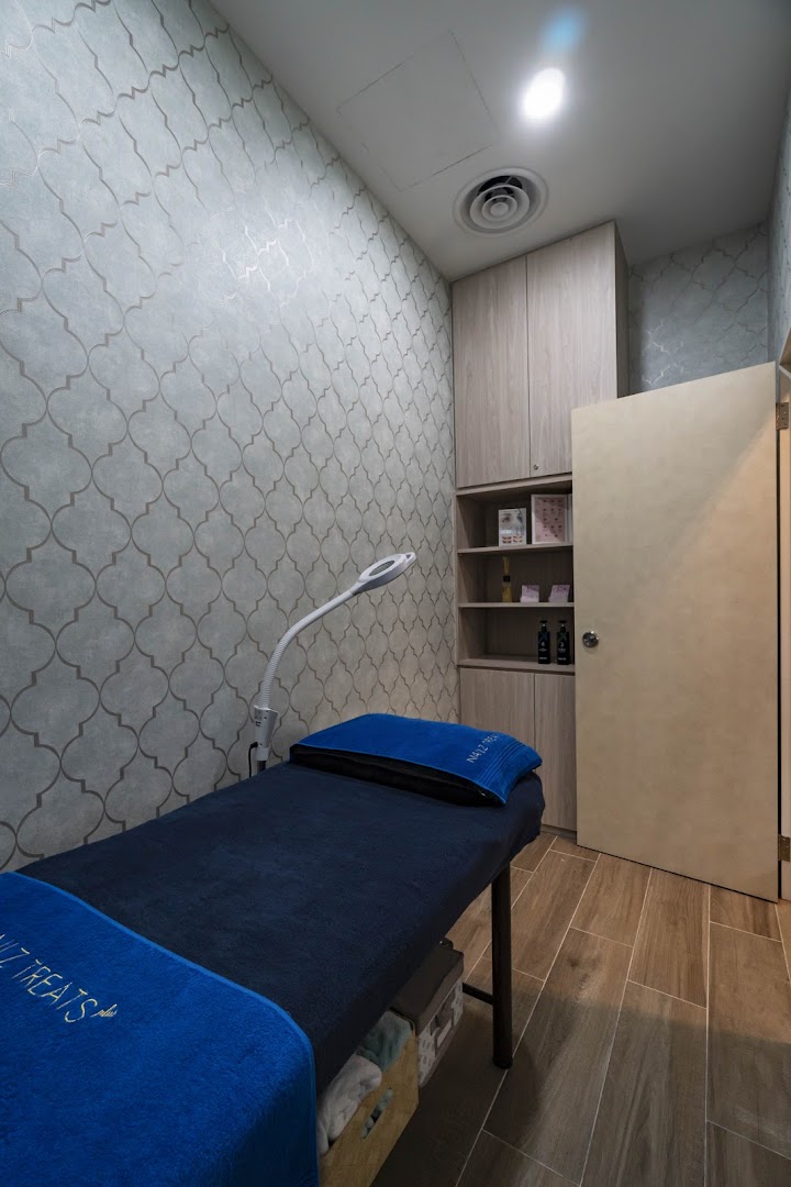 A cozy treatment room at Nailz Treats featuring a blue-covered bed and patterned wallpaper.