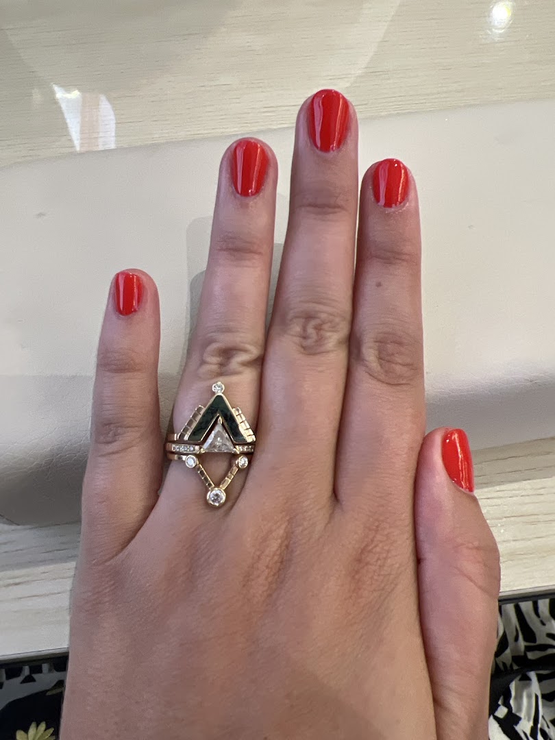 A hand with vibrant red nail polish and a unique gold ring, showcasing a fresh manicure.