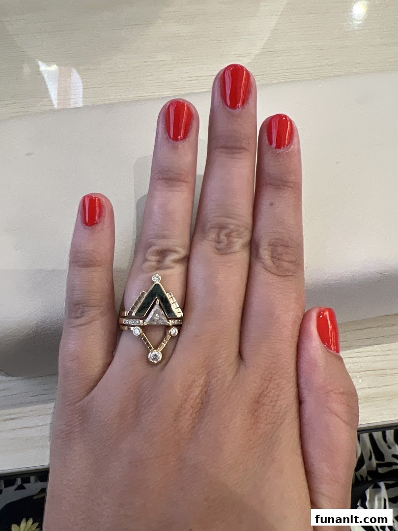 A hand with vibrant red nail polish and a unique gold ring, showcasing a fresh manicure.