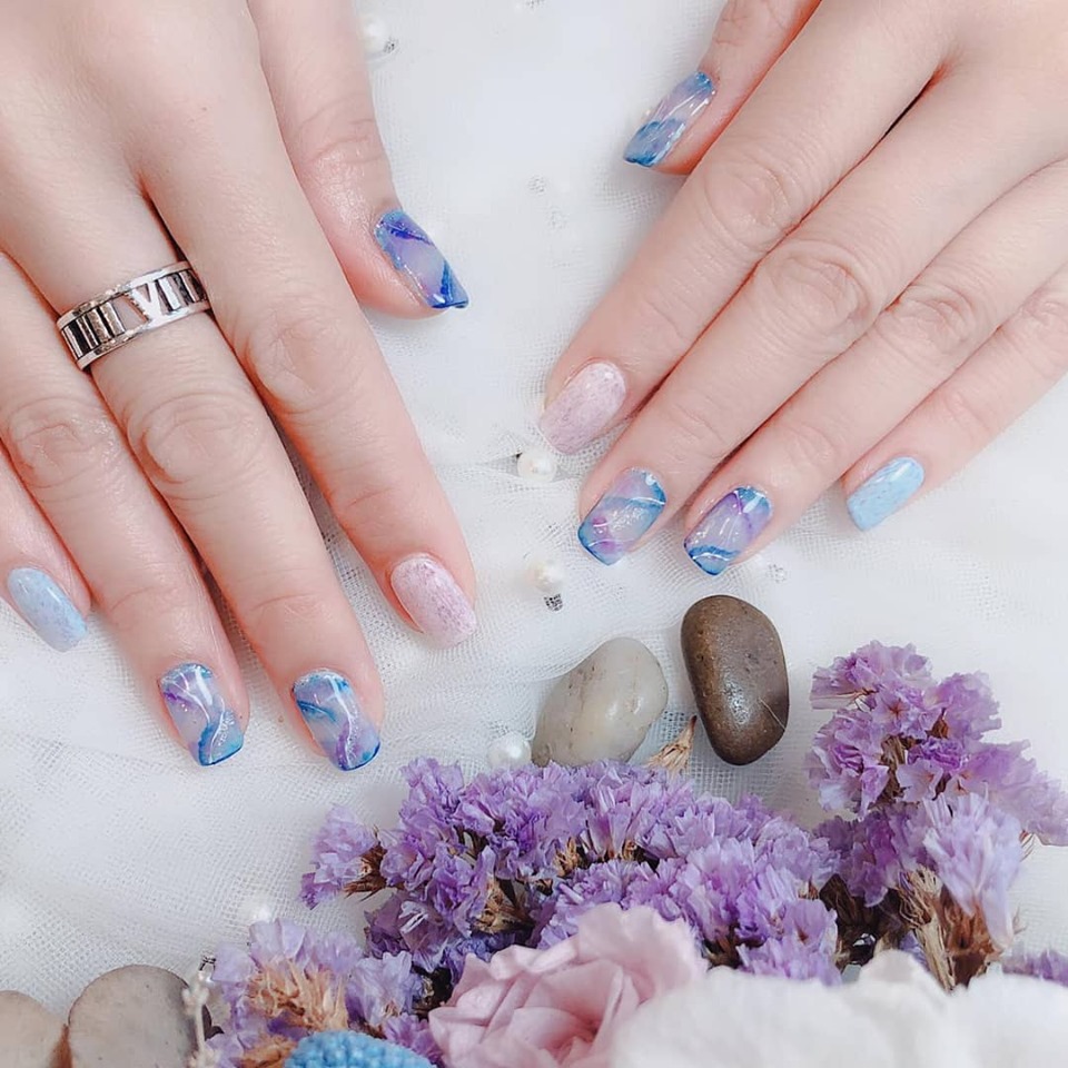 Close-up of hands showcasing intricate blue and purple marble nail art designs.