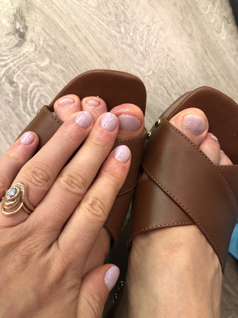 Close-up of feet in sandals and a hand, all with fresh, glittery light purple nail polish.
