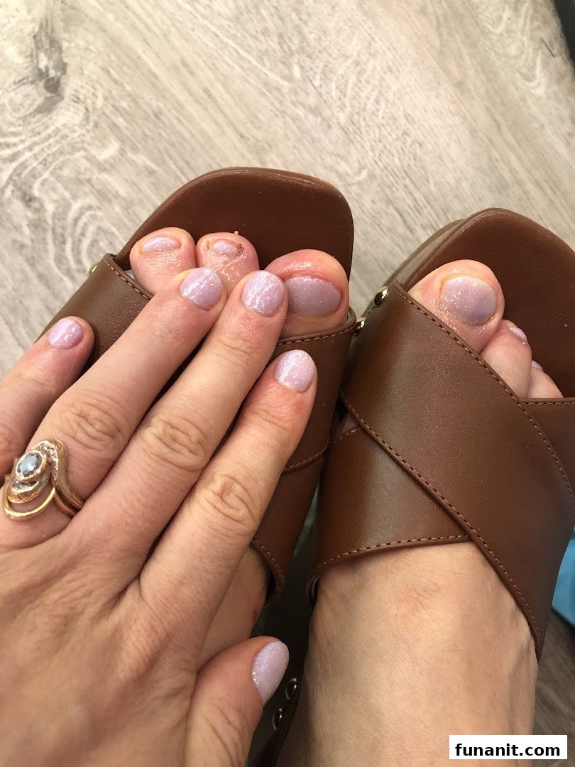 Close-up of feet in sandals and a hand, all with fresh, glittery light purple nail polish.