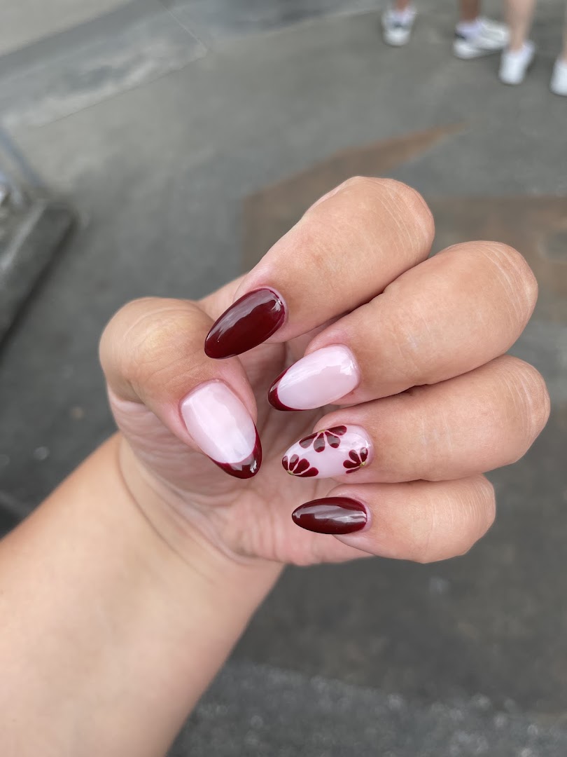 Close-up of a hand showcasing elegant maroon and nude manicured nails with floral accents.