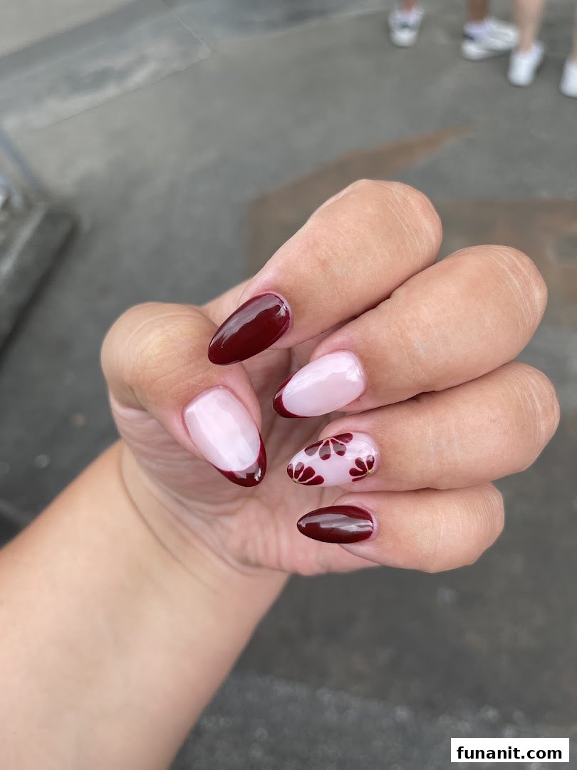 Close-up of a hand showcasing elegant maroon and nude manicured nails with floral accents.