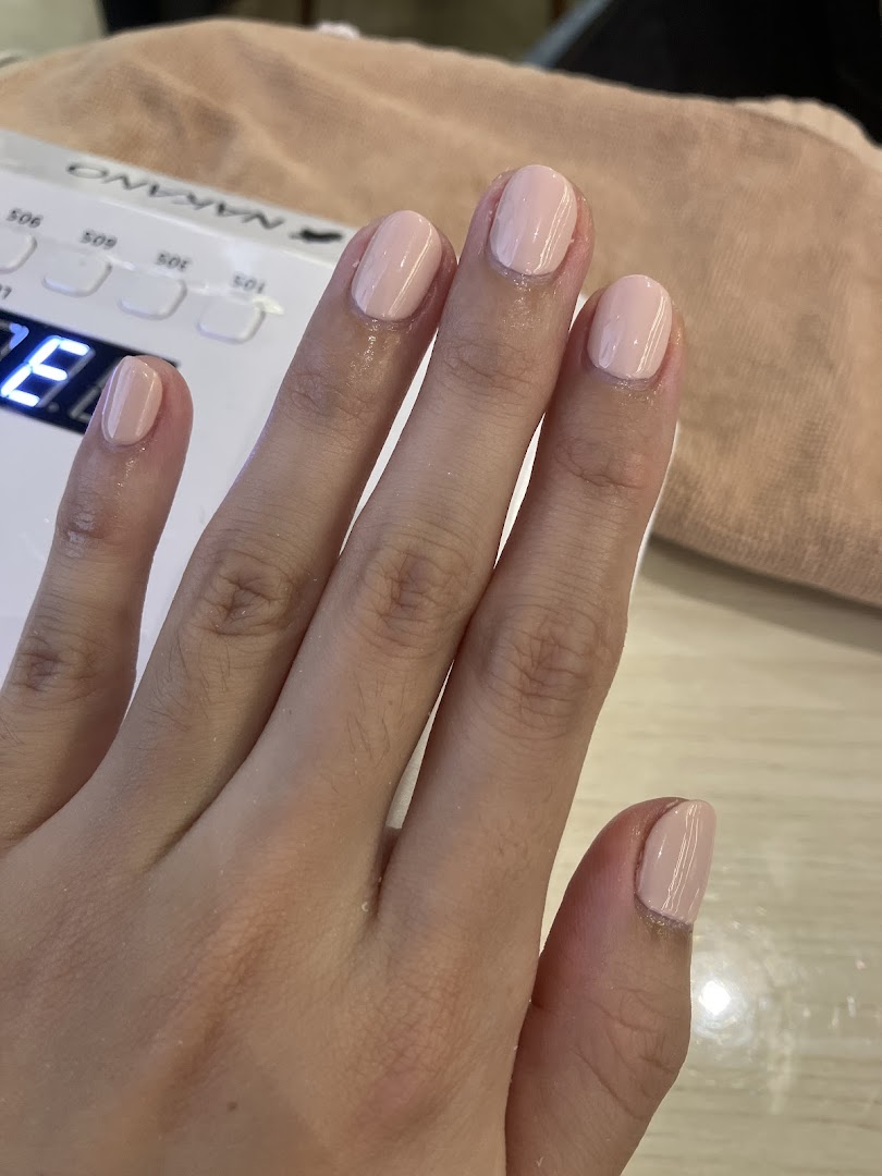 A hand with freshly painted light pink nails under a nail drying lamp.