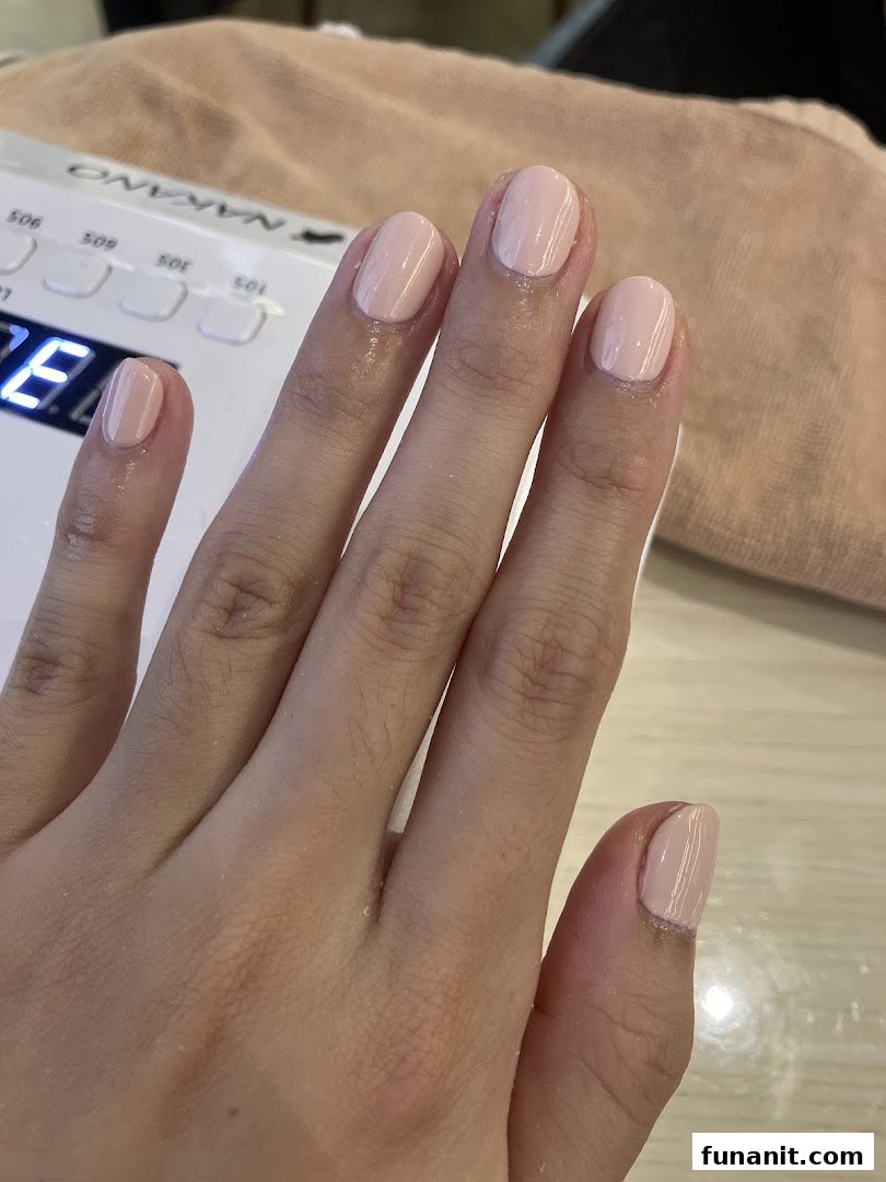 A hand with freshly painted light pink nails under a nail drying lamp.