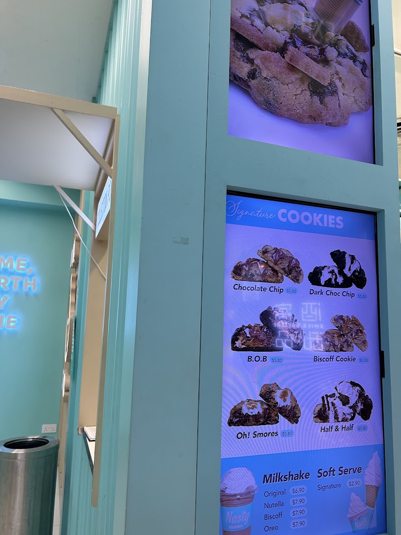 A digital menu board displaying signature cookies, milkshakes, and soft serve options with prices.