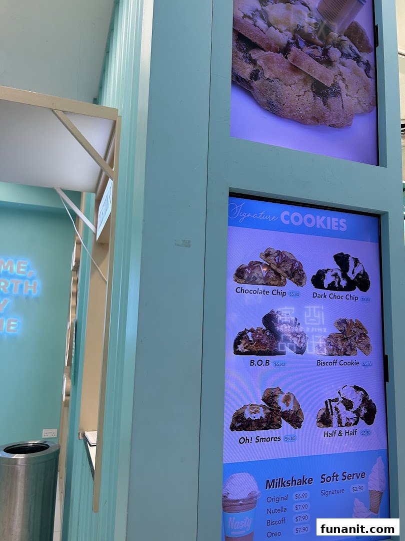 A digital menu board displaying signature cookies, milkshakes, and soft serve options with prices.