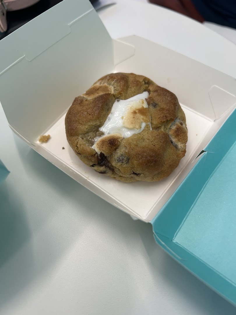 A large, delicious cookie with melted marshmallow and chocolate chips in a white box.