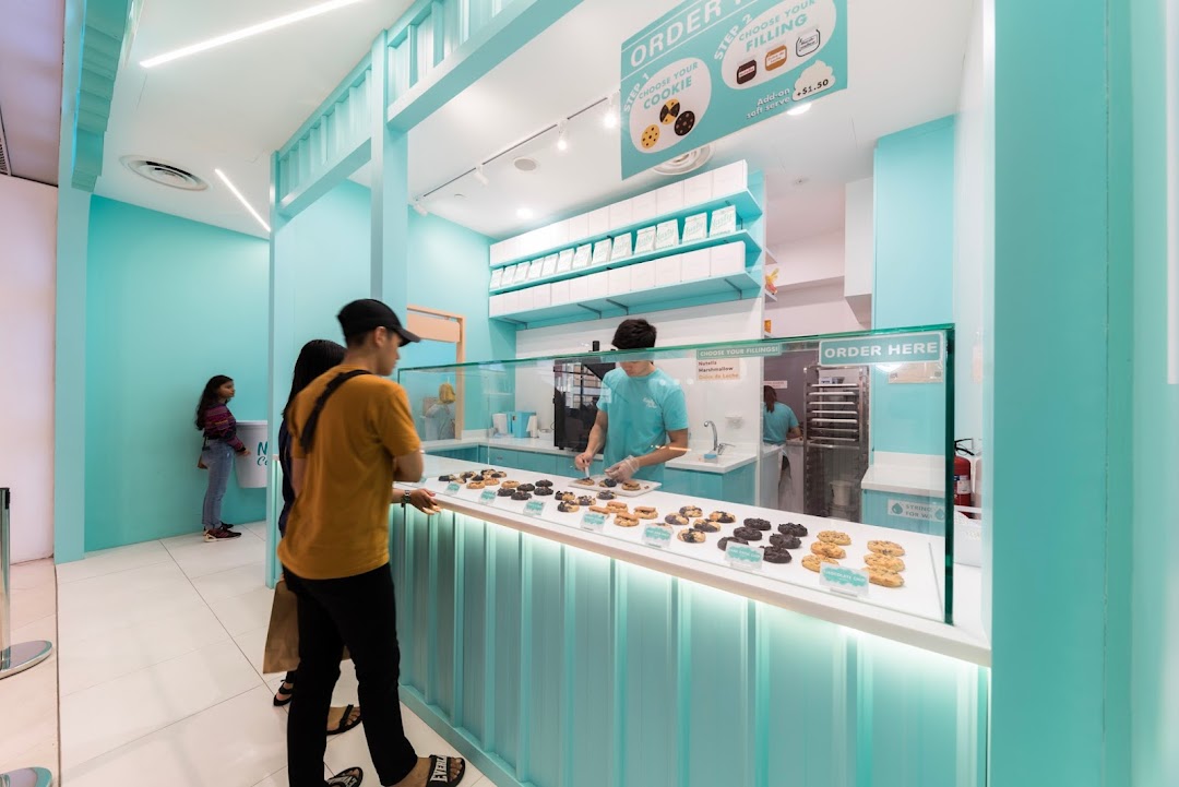 Customers order custom cookies at the vibrant, turquoise-themed Nasty Cookie shop counter.
