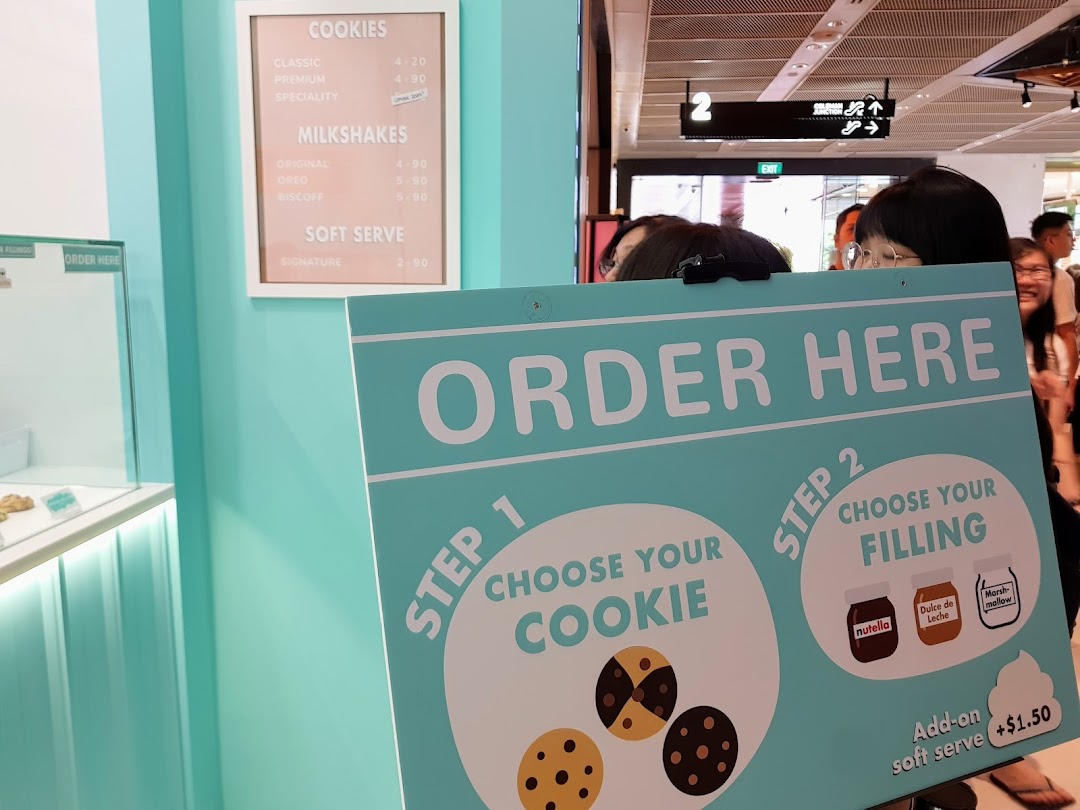 A vibrant shop interior featuring a menu board, 'Order Here' sign, and cookie customization options.