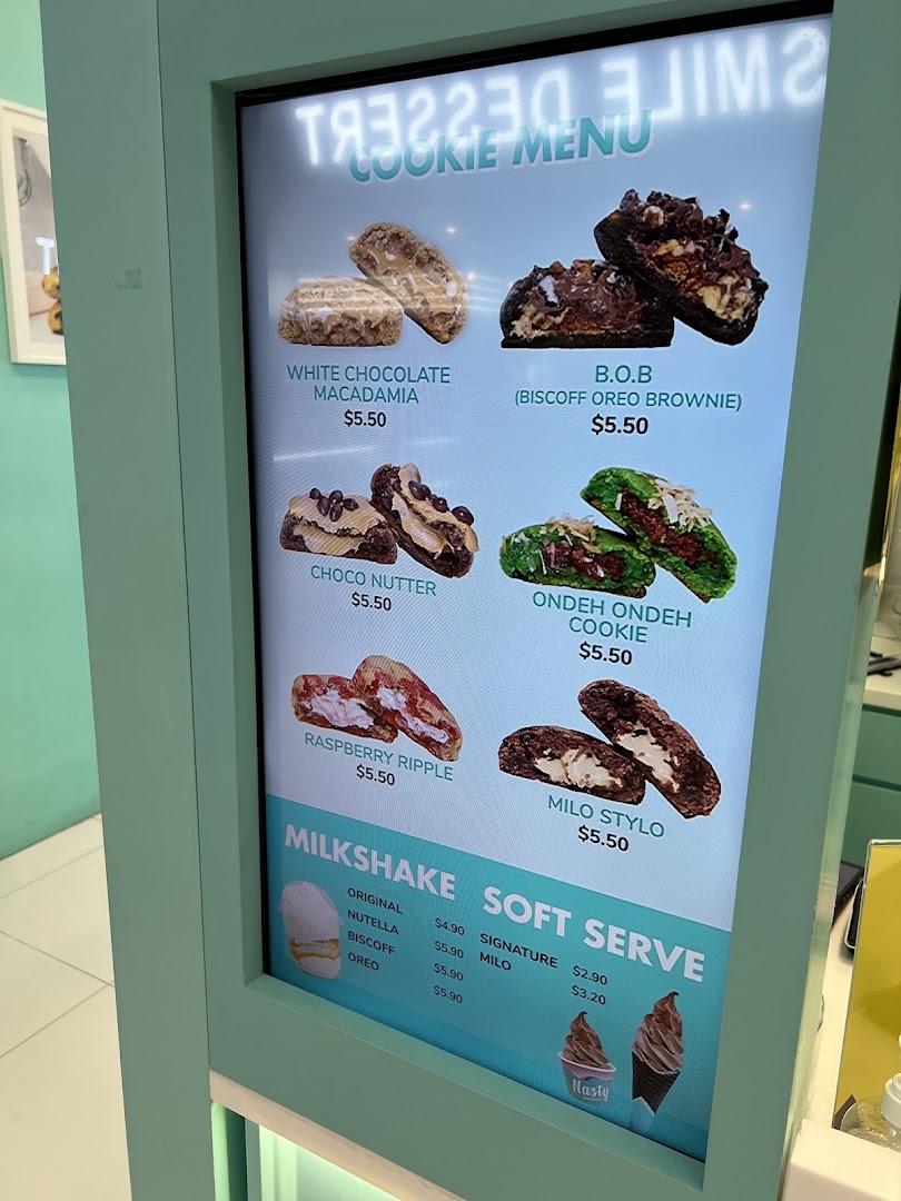 A digital menu board displaying various cookies, milkshakes, and soft serve options with prices.
