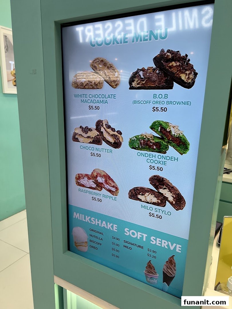 A digital menu board displaying various cookies, milkshakes, and soft serve options with prices.