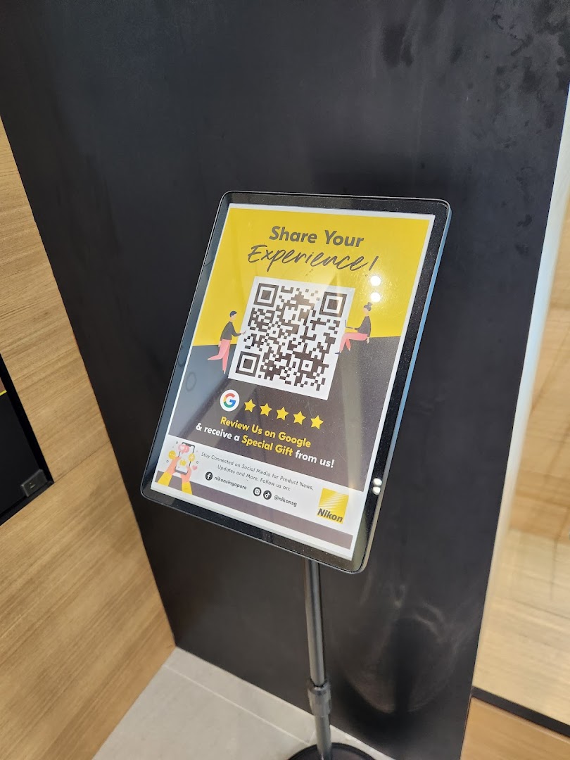 A stand-up sign inside the Nikon Experience Hub encouraging Google reviews and social media engagement.