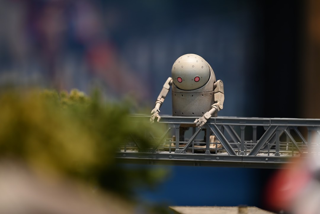 A detailed miniature robot figure with red eyes stands on a model bridge, showcasing intricate detail.