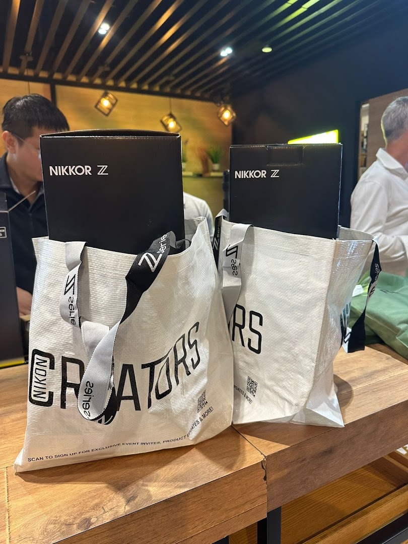 Two Nikon-branded shopping bags with NIKKOR Z product boxes on a wooden counter inside the store.