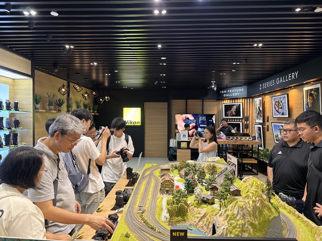 Visitors engage with Nikon cameras at an interactive display featuring a miniature landscape and product galleries.