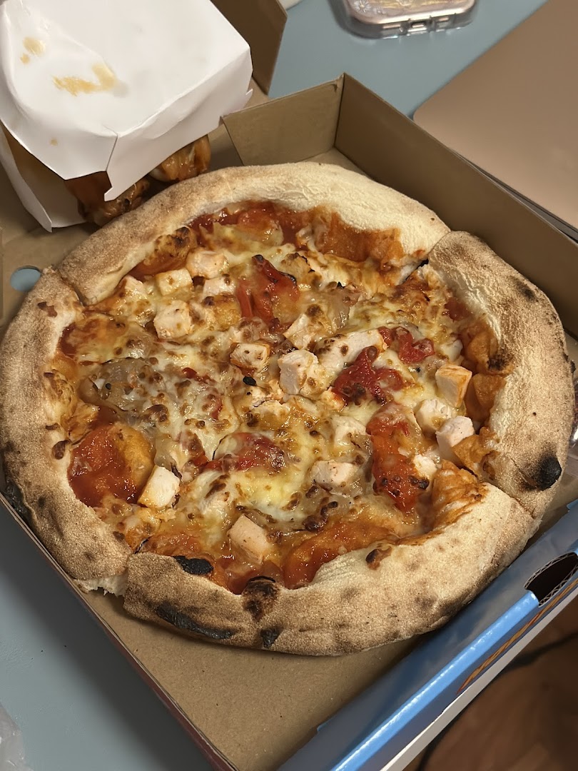 A close-up of a delicious-looking pizza with chicken and tomatoes in a takeout box.