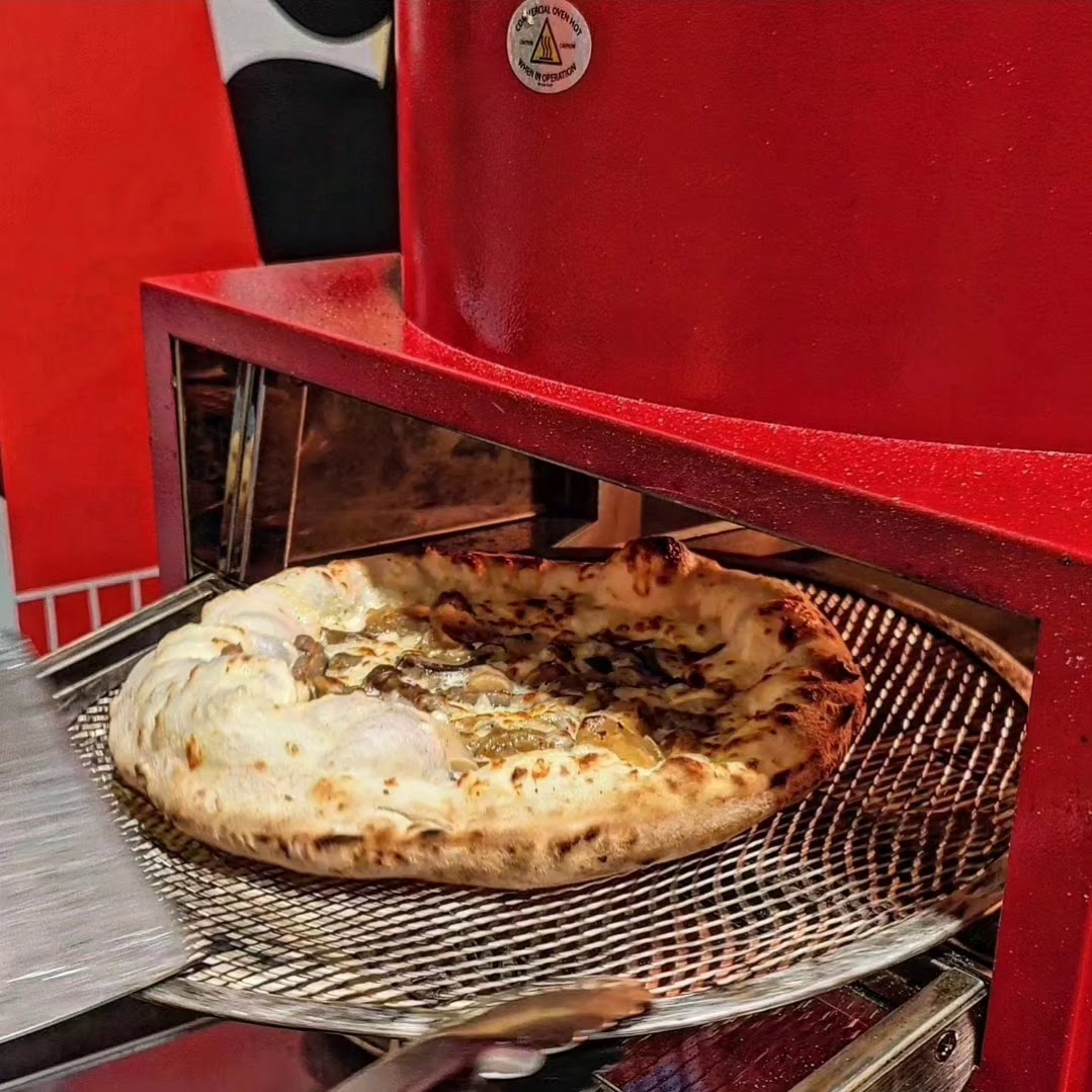 A freshly baked pizza with a golden crust being removed from a red commercial oven.