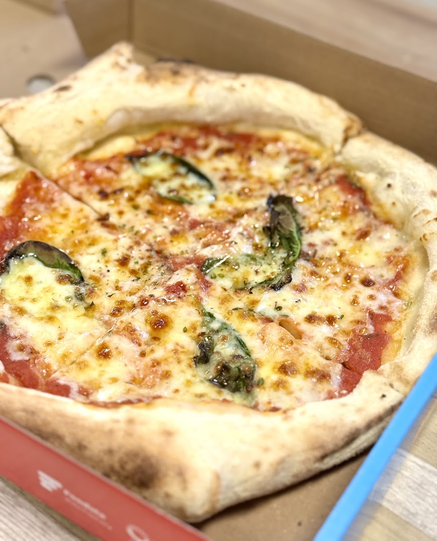 A freshly baked pizza with melted cheese and basil in a delivery box.