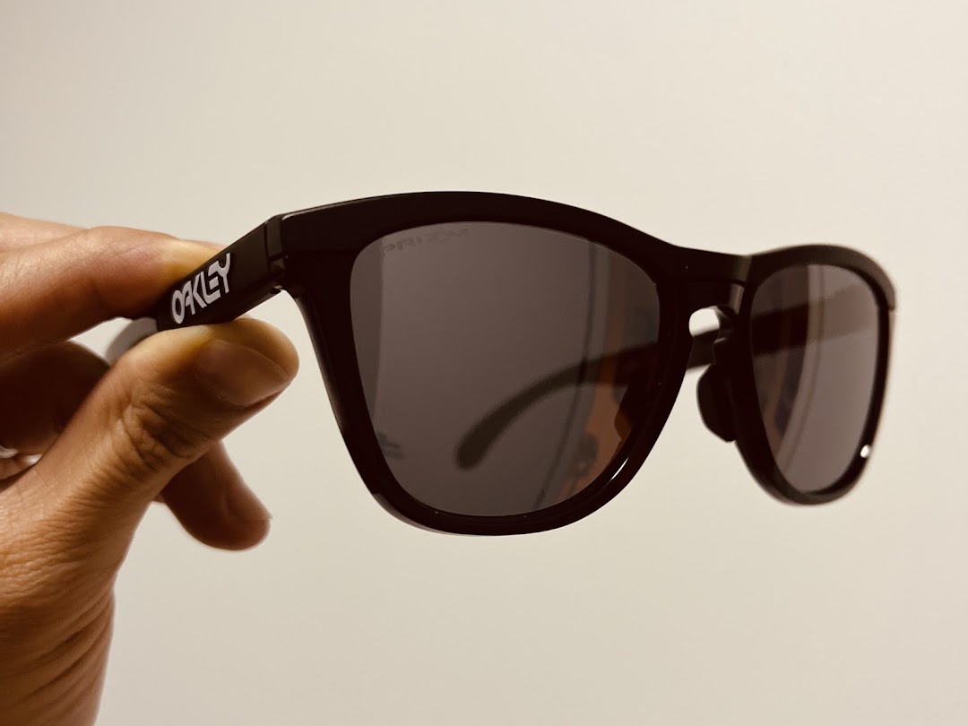 A hand holds a pair of black Oakley Prizm sunglasses, showcasing the brand logo.