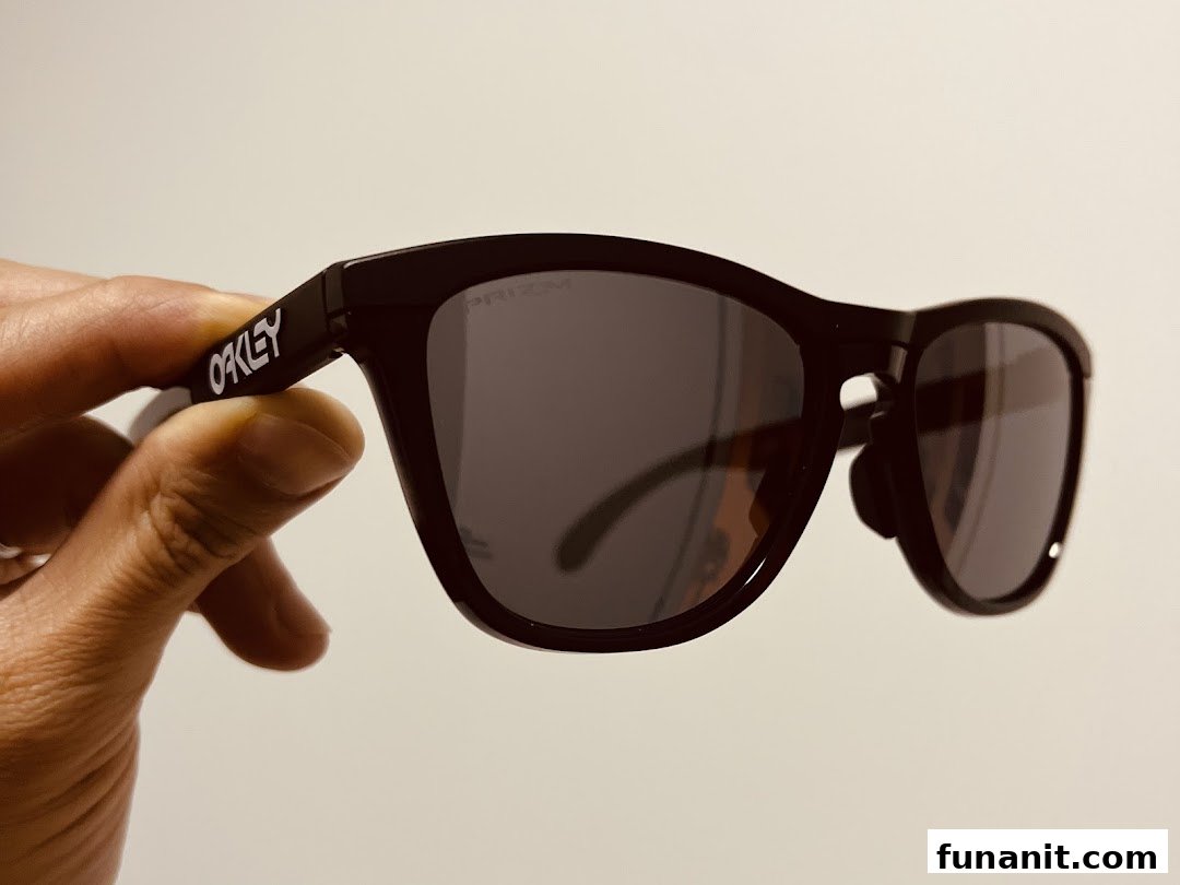 A hand holds a pair of black Oakley Prizm sunglasses, showcasing the brand logo.