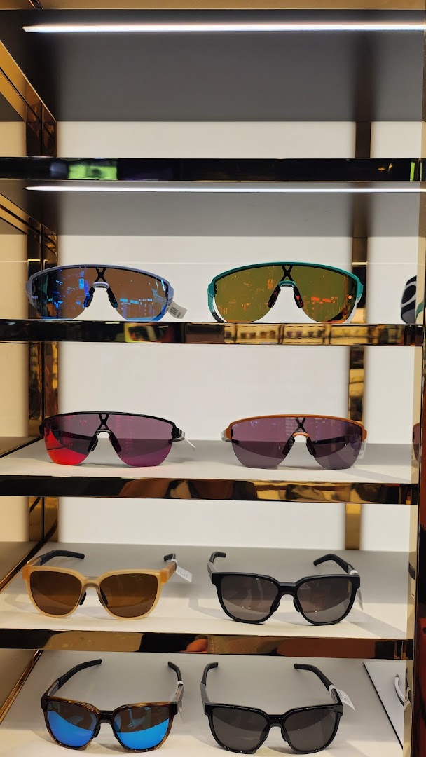 A display of various Oakley sunglasses with different frame and lens colors on white shelves.