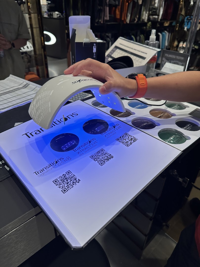 A hand demonstrates Transitions lens technology with a UV light at an Oakley store display.