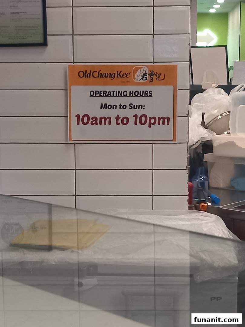 A sign at Old Chang Kee displaying the shop's daily operating hours.