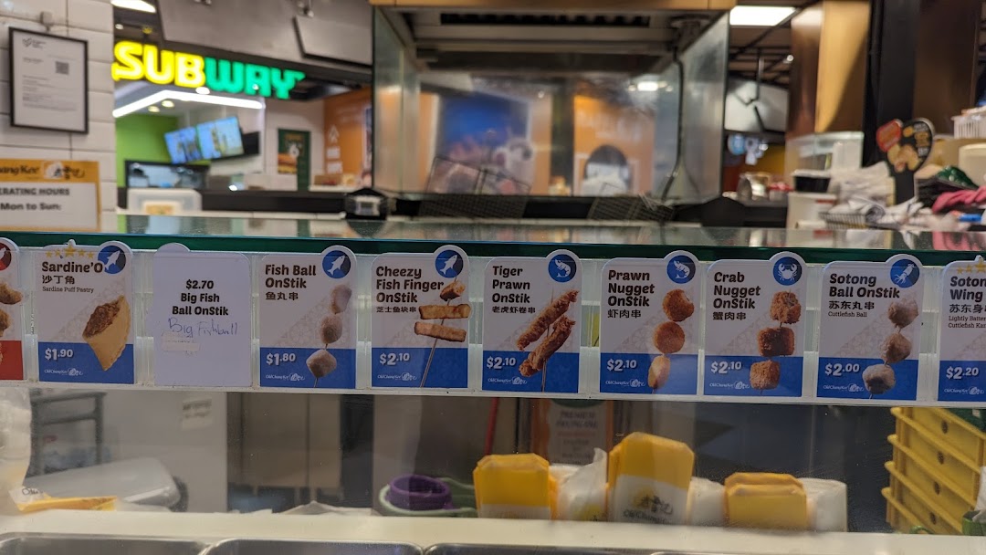 A display of various fried snacks on sticks and pastries with prices at Old Chang Kee.