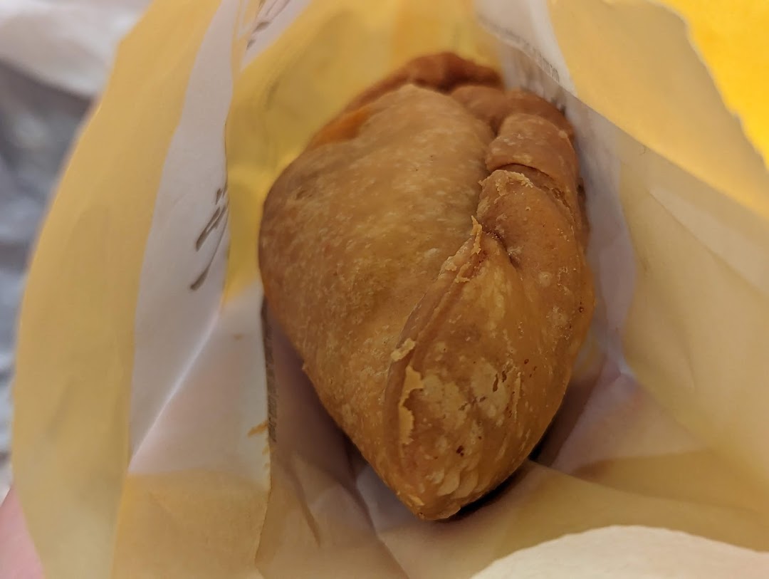 A golden-brown curry puff peeking from a paper bag, ready to be enjoyed.