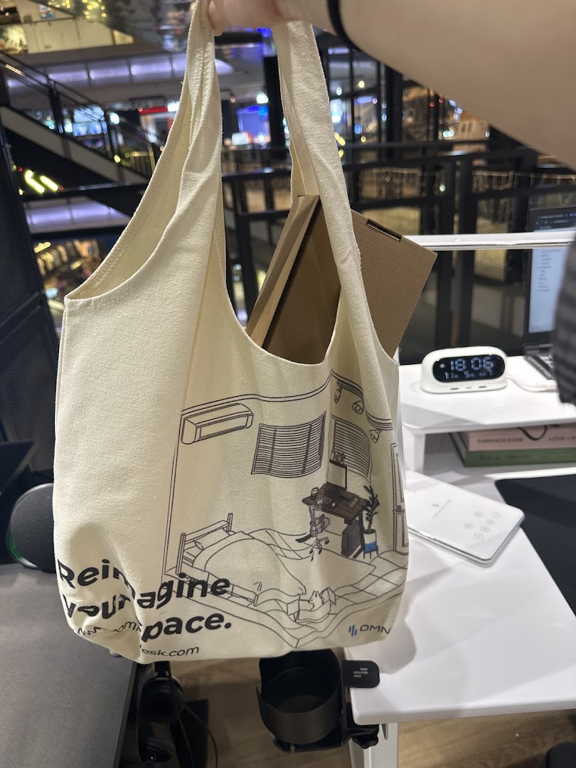 A person holds an Omnidesk branded tote bag featuring a home office illustration inside the store.