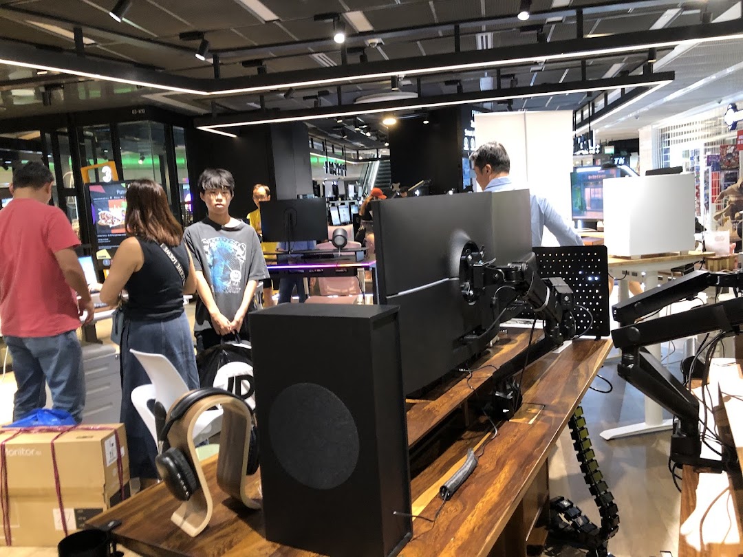 Customers browse ergonomic desks and tech accessories like monitors, speakers, and headphones at Omnidesk Funan Mall.