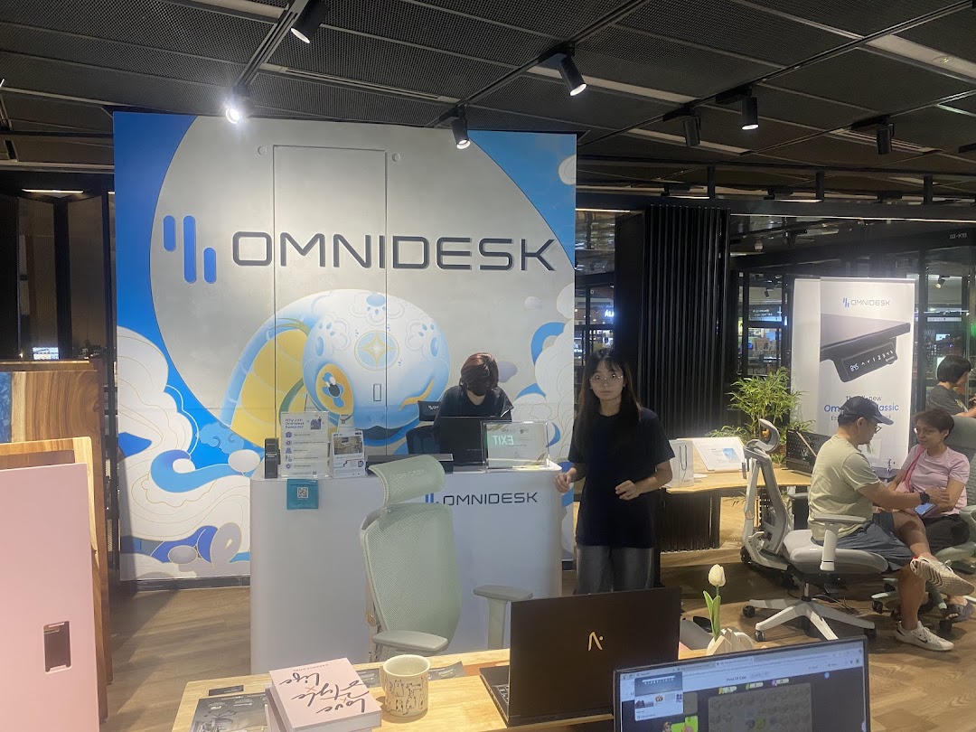 Interior view of Omnidesk Funan Mall, showcasing ergonomic desks and chairs with staff assisting customers.