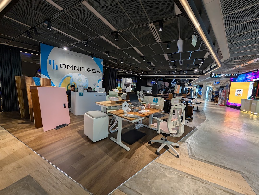 Interior view of Omnidesk Funan Mall, showcasing ergonomic standing desks, office chairs, and a reception area.