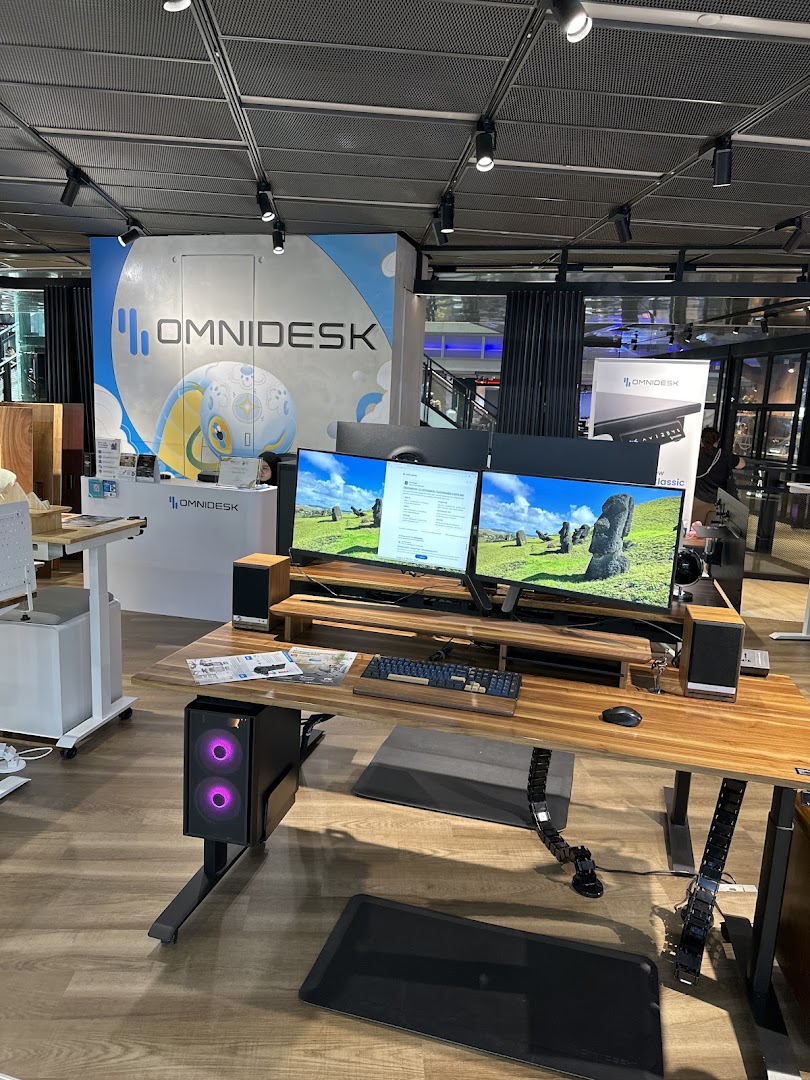 An Omnidesk display setup featuring an ergonomic desk, dual monitors, and a gaming PC in a modern showroom.