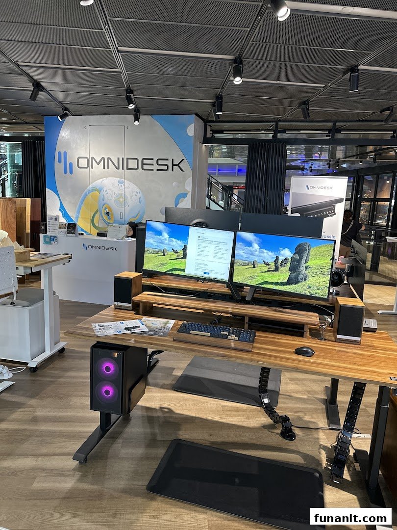 An Omnidesk display setup featuring an ergonomic desk, dual monitors, and a gaming PC in a modern showroom.
