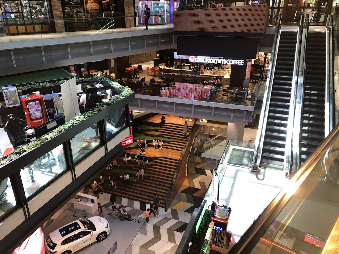 Overhead view of a bustling multi-level shopping mall interior with shops, escalators, and a central seating area.
