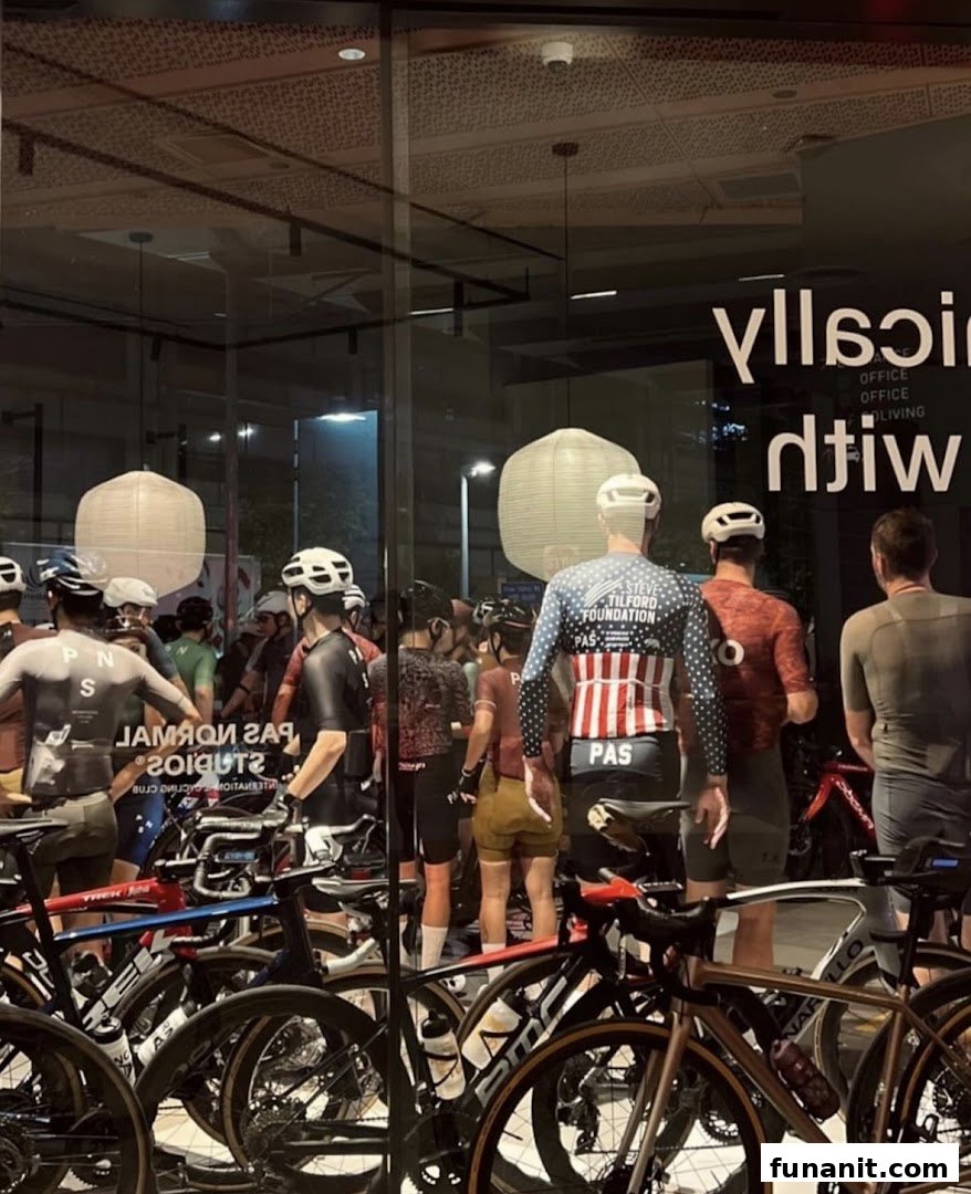 Cyclists and high-end bicycles are displayed inside Pas Normal Studios, viewed through a glass window.