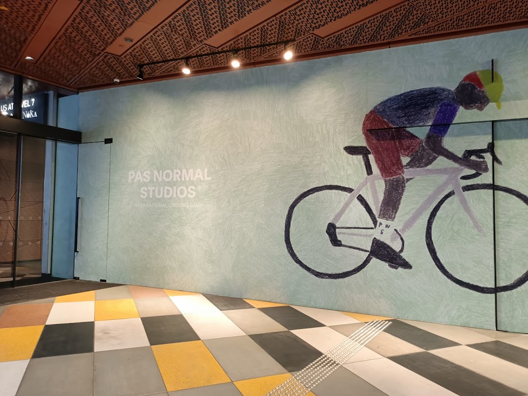 The entrance of Pas Normal Studios Singapore featuring a large cyclist mural and brand signage.