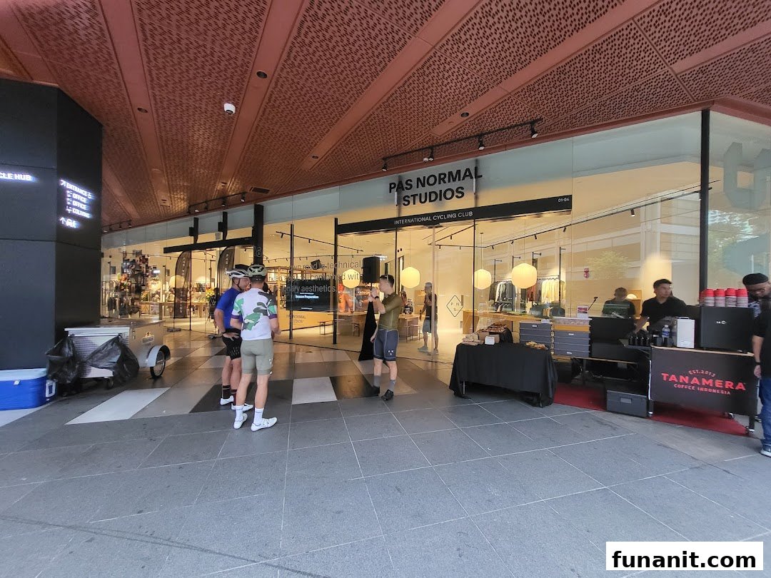 The shopfront of Pas Normal Studios, an International Cycling Club, with cyclists and a coffee stand outside.